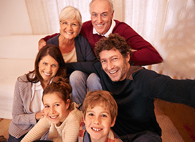 A multi-generational family posing together with smiles in a cozy living room setting.